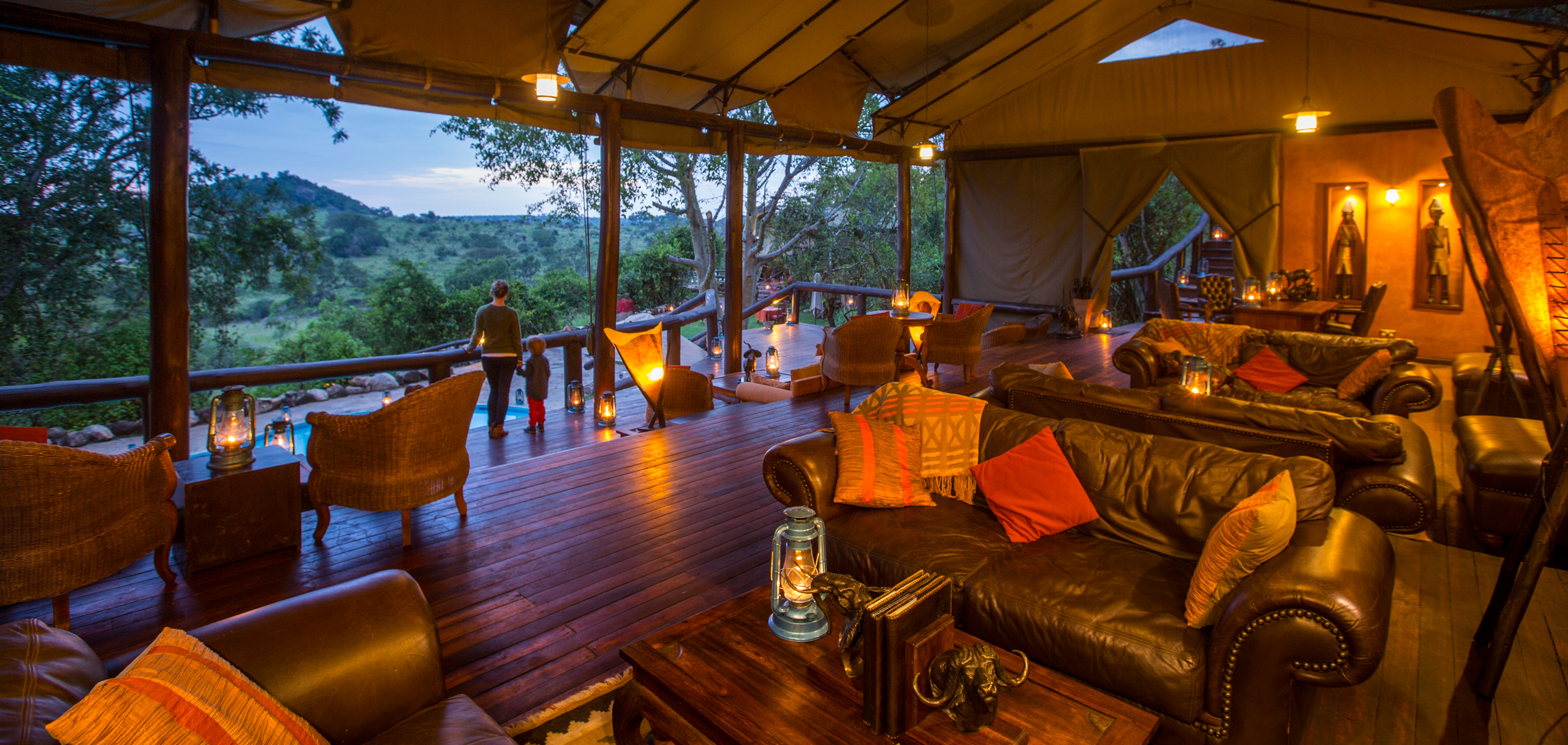 Open-fronted lounge furnished in dark wood and leather, with views over the neighbouring kopje