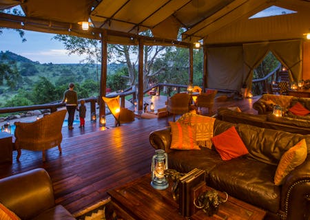 Open-fronted lounge furnished in dark wood and leather, with views over the neighbouring kopje