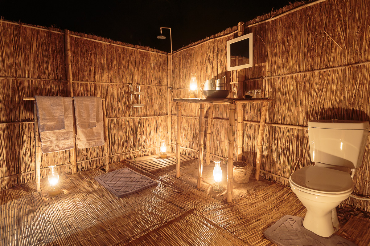 Open-air en-suite bathroom with plumbed lavatory and sink, hot bucket showers and guest amenities